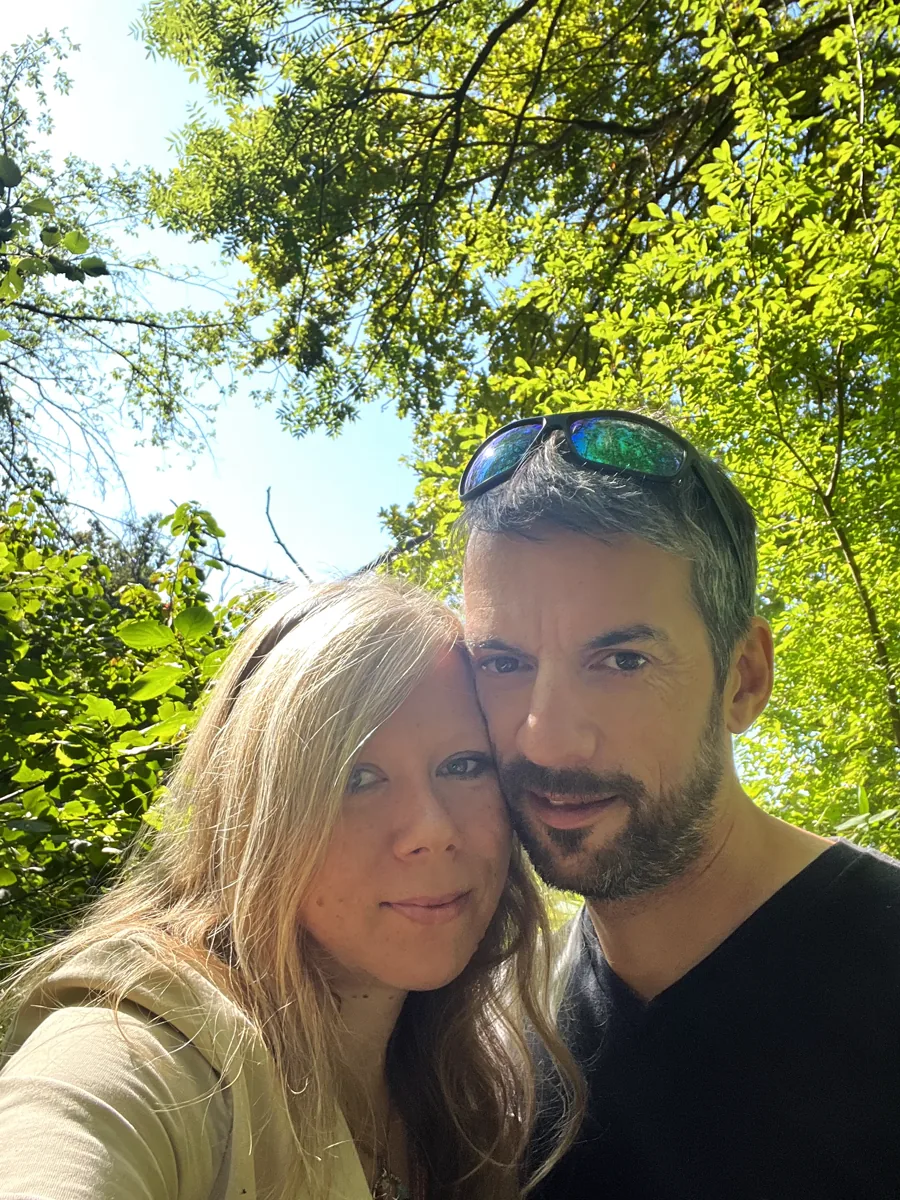Cindy Streeck und ihr Mann Charly Wange an Wange unter sonnendurchfluteten Bäumen